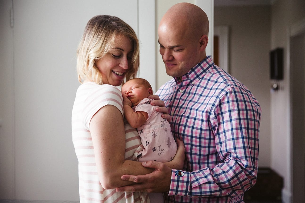 A documentary photograph of new parents smiling at their sleeping newborn baby during their in home lifestyle session in Boston, Massachusetts