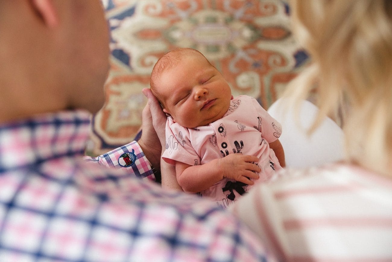 A documentary photograph of new parents admiring their sleeping newborn daughter during an in home lifestyle session in Boston, Massachusetts