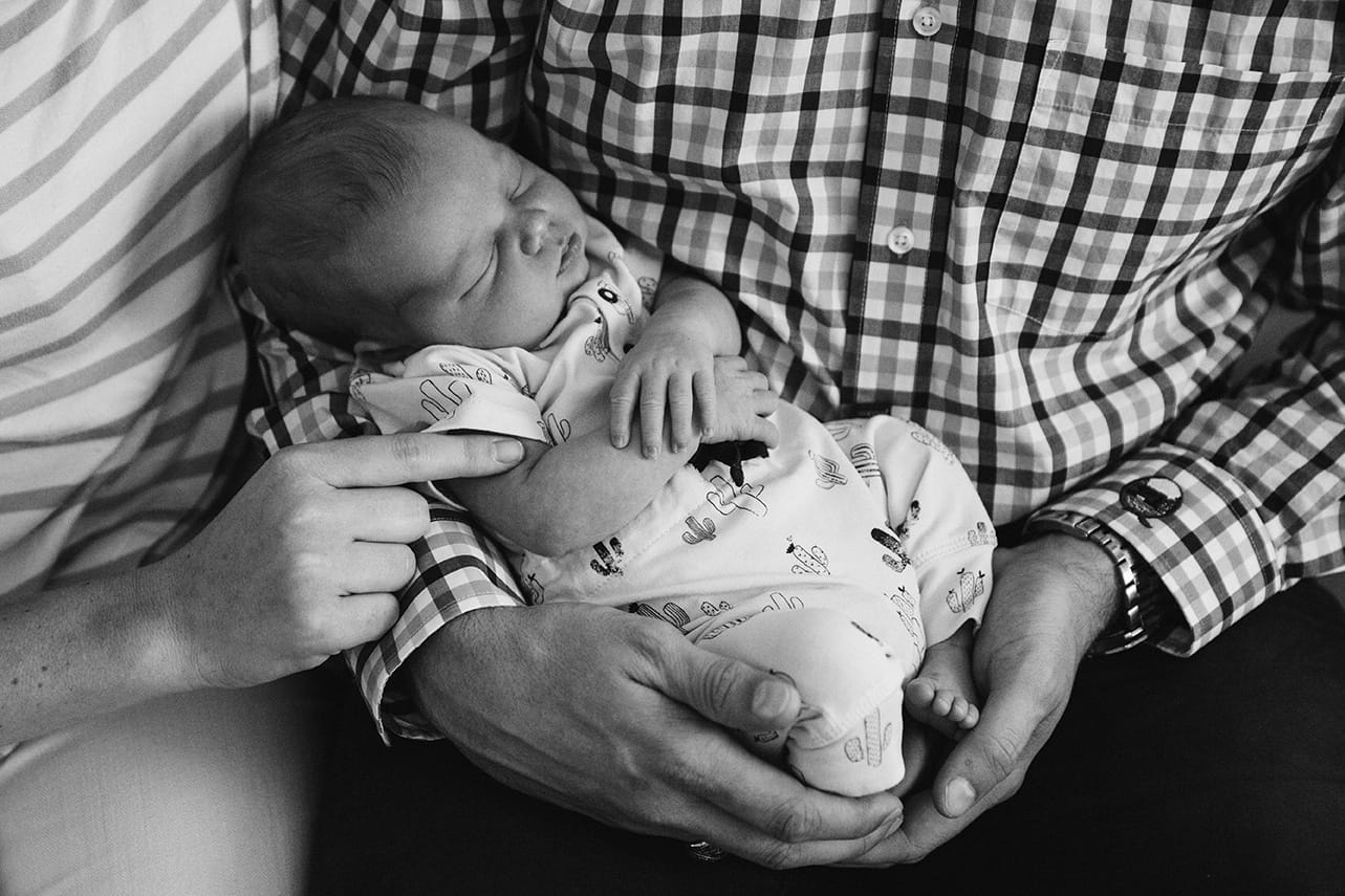 A documentary photograph of new parents holding their sleeping newborn daughter during an in home lifestyle session in Boston, Massachusetts