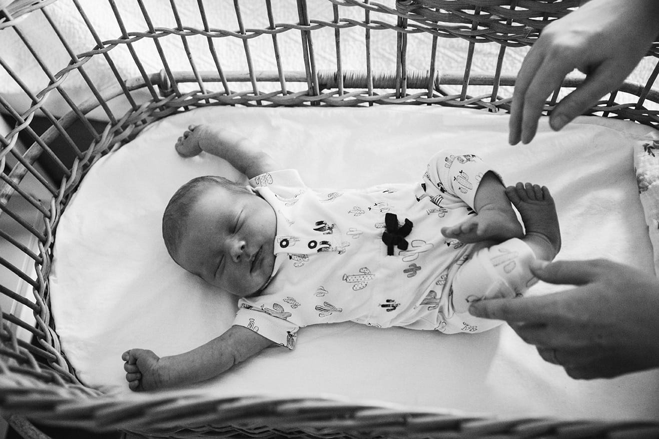 A documentary photograph of a father putting his sleeping newborn daughter in a bassinet during their in home lifestyle session in Boston, Massachusetts