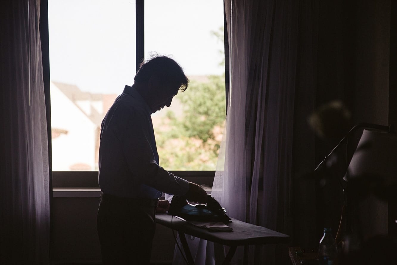 A documentary photograph of the groom's father ironing his shirt before his plimoth plantation wedding in plymouth, massachusetts