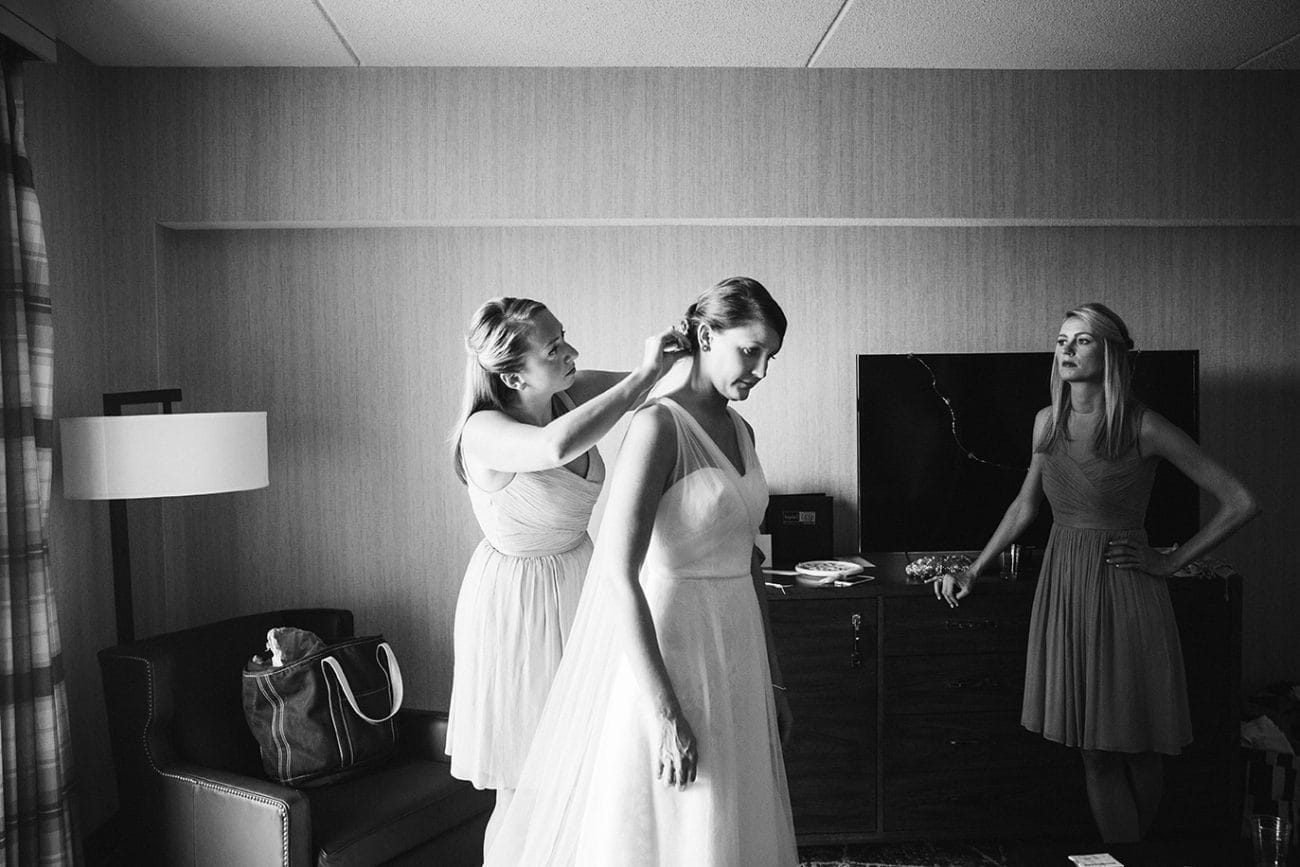 A documentary photograph of a bridesmaid putting the veil on the bride before her plimoth plantation wedding in plymouth, massachusetts