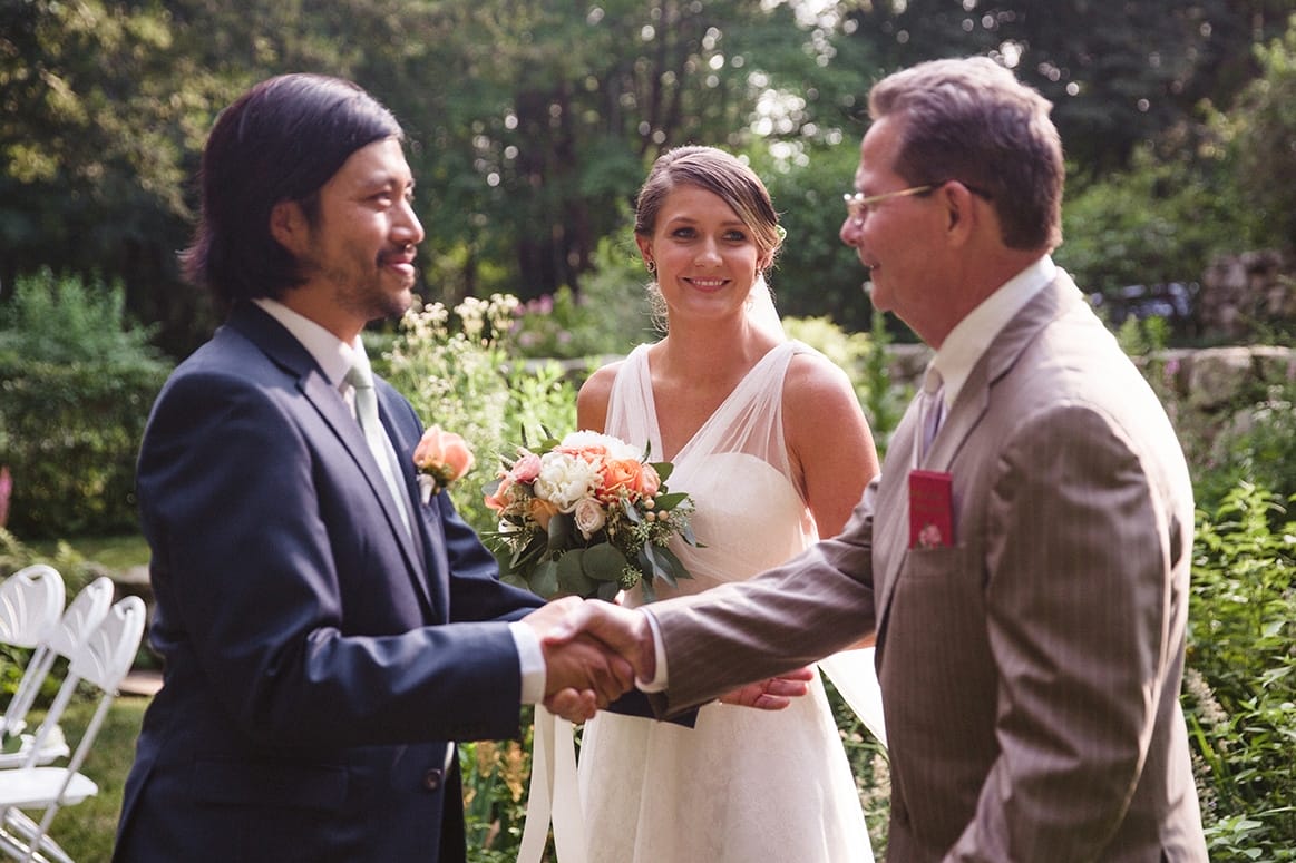 A documentary photograph of a bride smiling as her father shakes the hand of her groom during their plimoth plantation wedding in plymouth, massachusetts