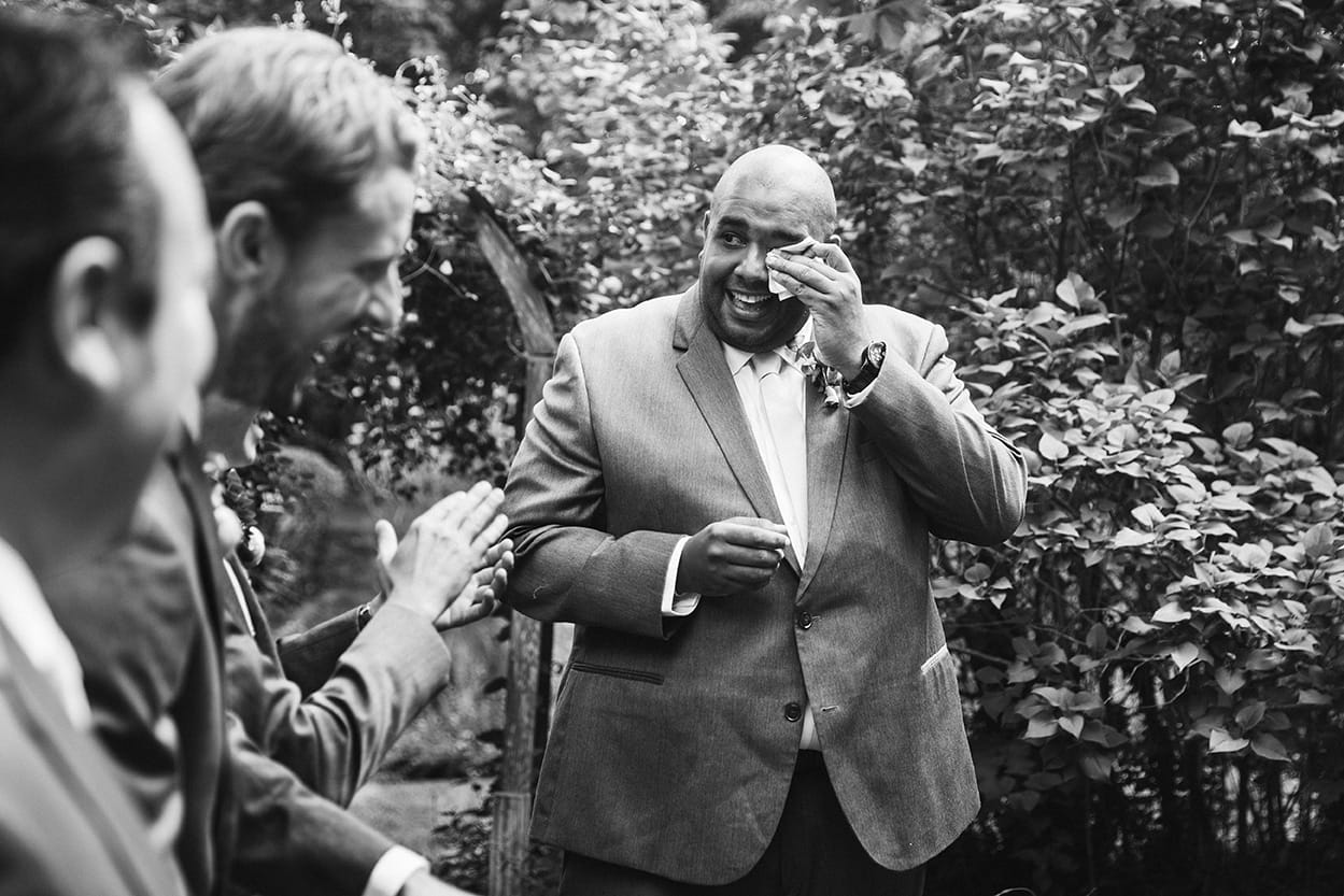 A documentary photograph of a groomsman wiping away tears moments after an outdoor plimoth plantation wedding ceremony in plymouth, massachusetts