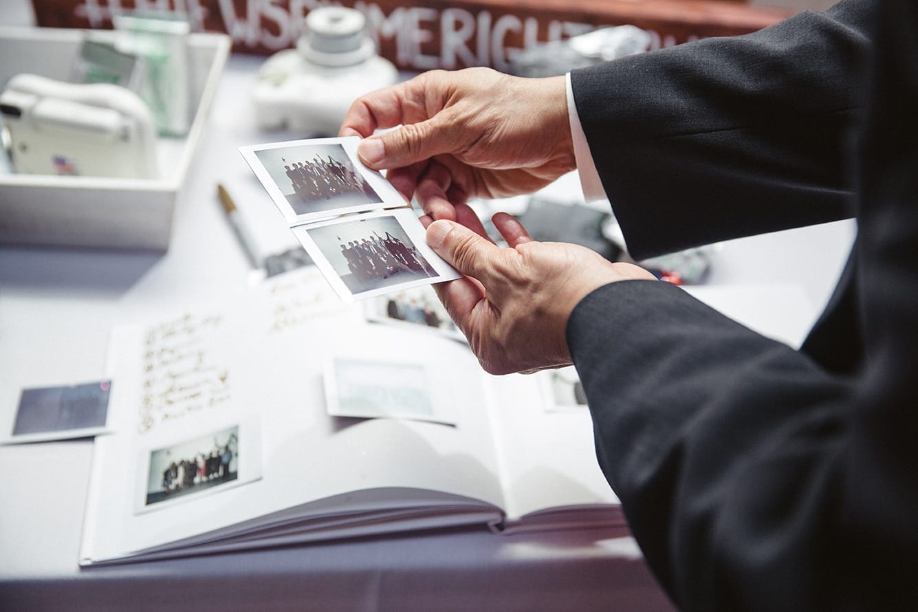 A documentary photograph of a guest comparing polaroid pictures during a plimoth plantation wedding in plymouth, massachusetts