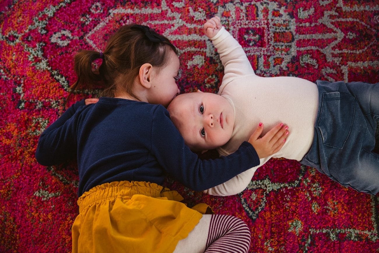 A documentary portrait of a big sister kissing her baby brother during their in home family lifestyle session in Boston, Massachusetts