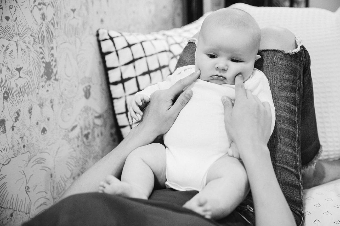 A documentary photograph of a mom poking her baby boy's cheeks during an in home family lifestyle session in Boston, Massachusetts