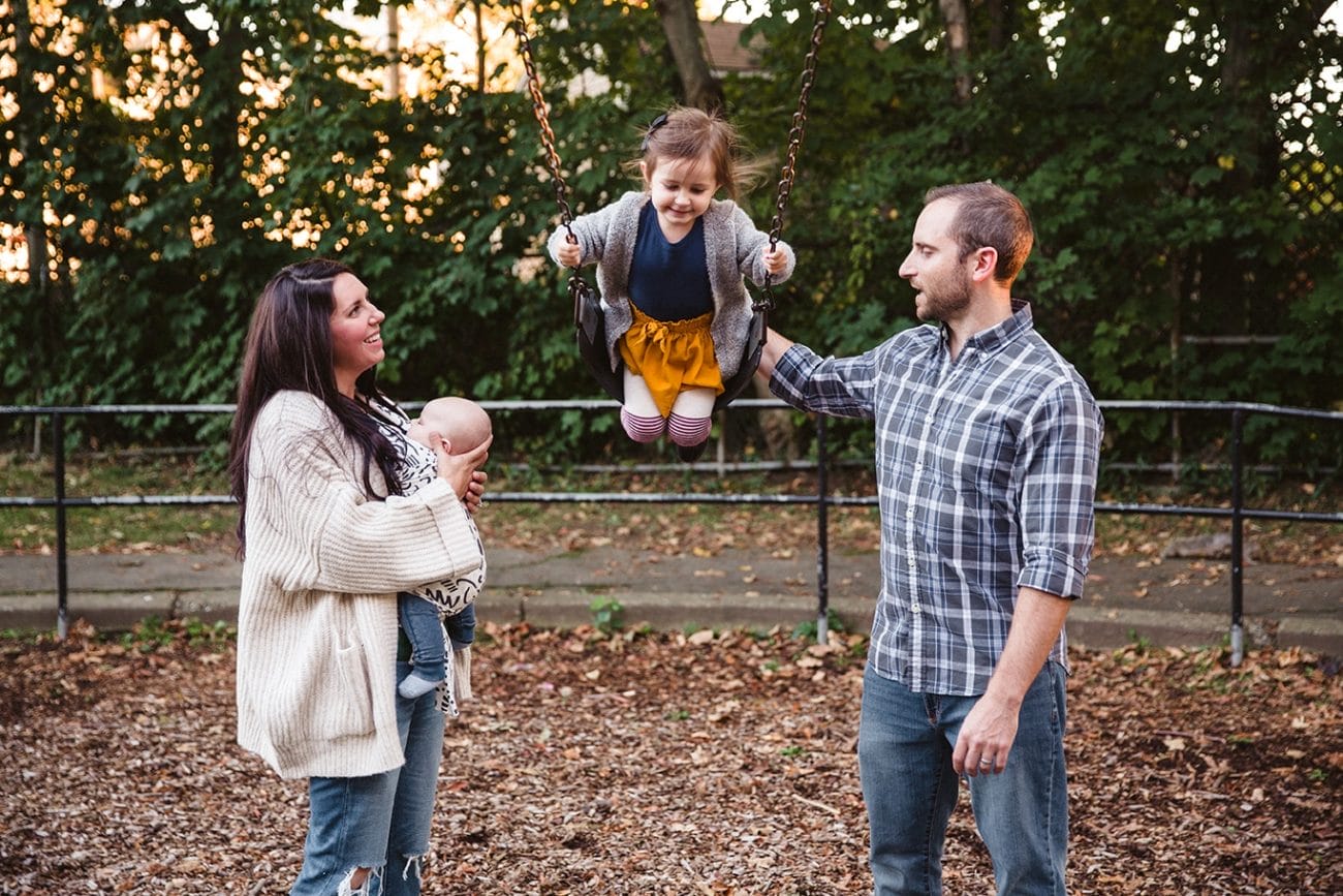 A documentary photograph of mom and dad pushing their daughter on the swings during their family lifestyle session in Boston, Massachusetts