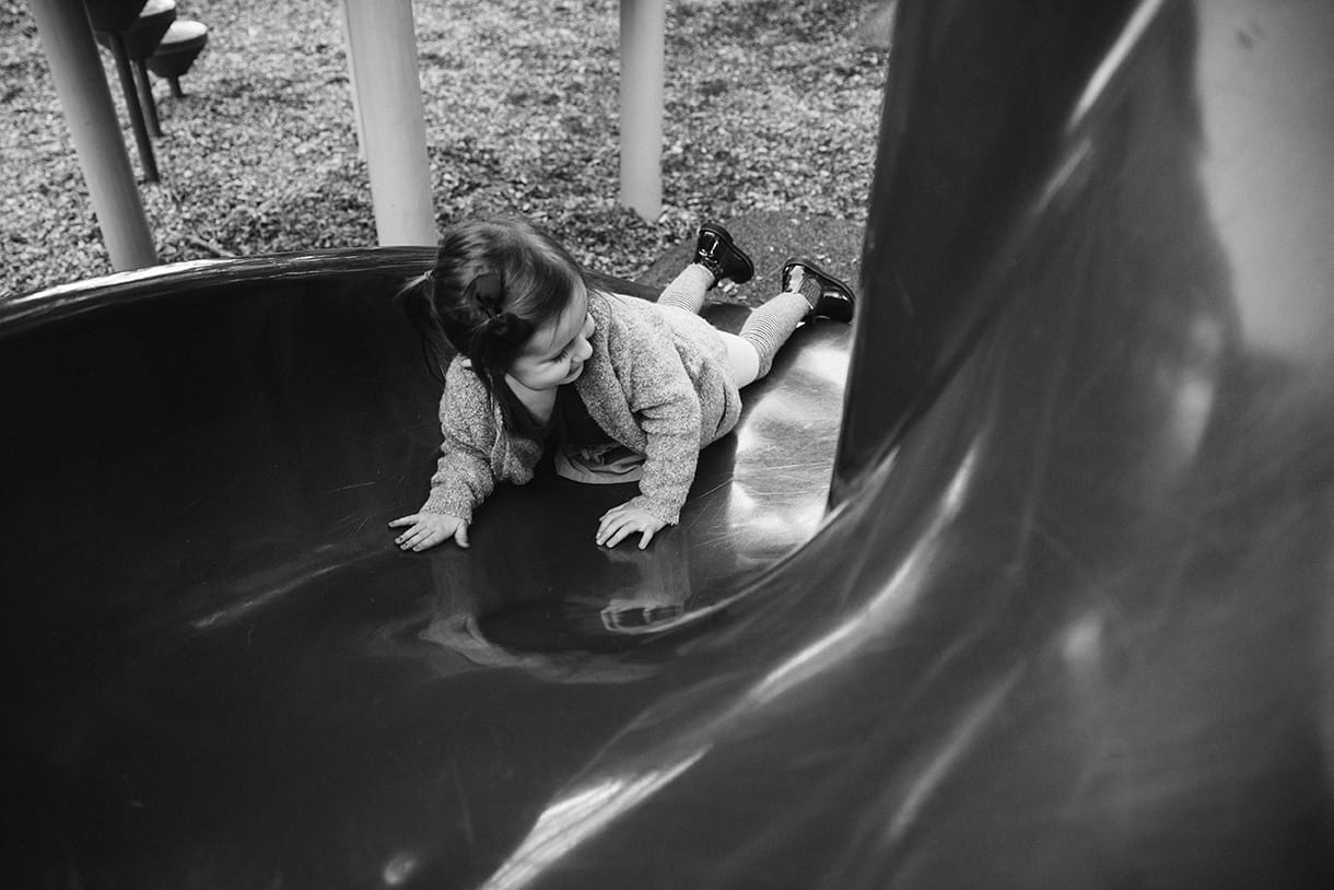 A documentary photograph of a little girl sliding down a slide at the playground during a family lifestyle session in Boston, Massachusetts