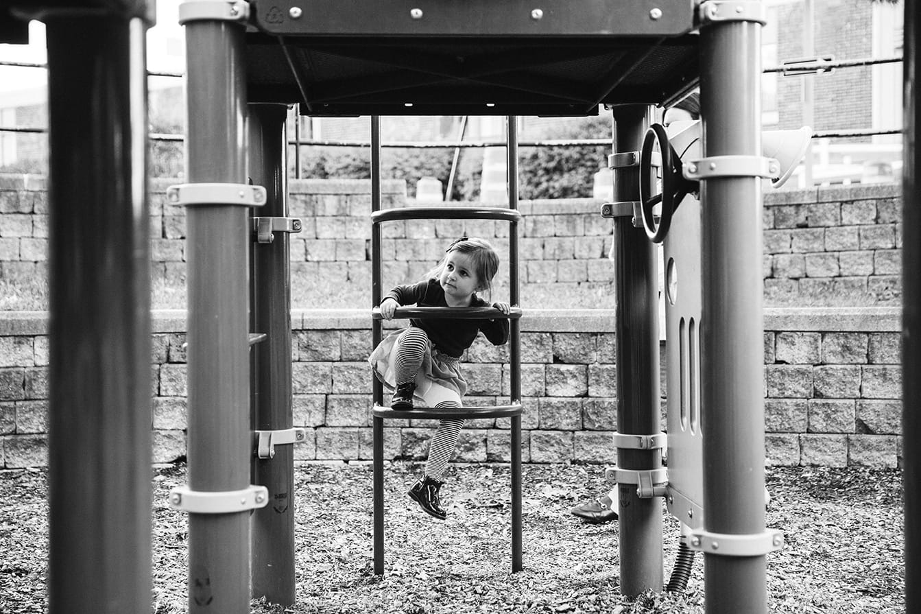 A documentary photograph of a little girl climbing a ladder at the playground during a family lifestyle session in Boston, Massachusetts
