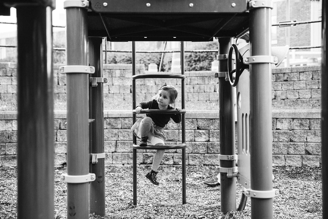 A documentary photograph of a little girl climbing a ladder at the playground during a family lifestyle session in Boston, Massachusetts