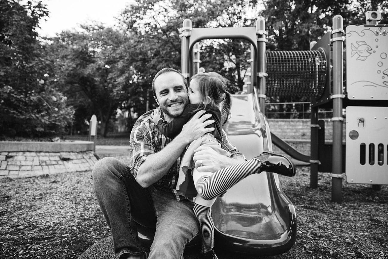 A documentary photograph of a little girl giving her dad a kiss at the playground during a family lifestyle session in Boston, Massachusetts