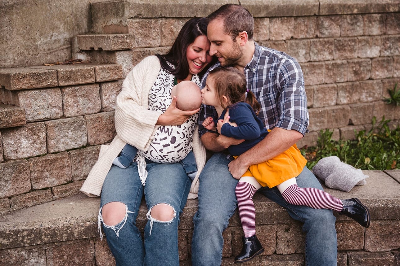 A documentary photograph of a big sister kissing her baby brother at the playground during a family lifestyle session in Boston, Massachusetts