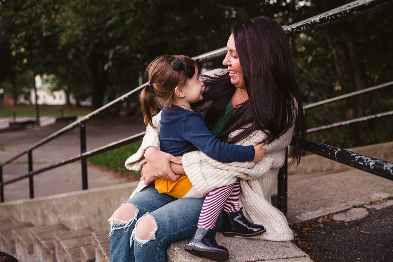 A documentary photograph of a daughter sitting on her mom's lap at the playground during a family lifestyle session in Boston, Massachusetts