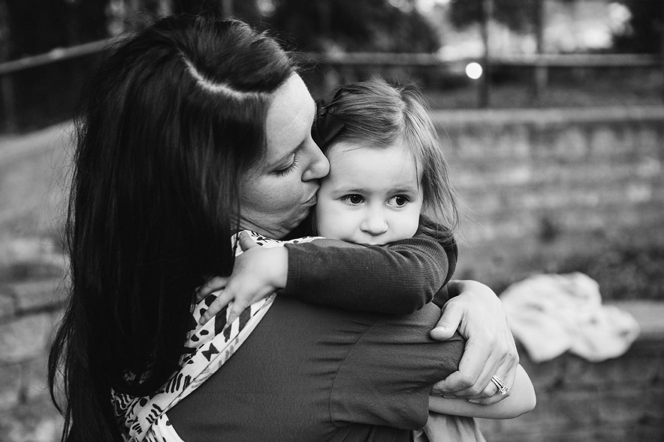 A documentary photograph of a mom kissing her daughter at the playground during a family lifestyle session in Boston, Massachusetts