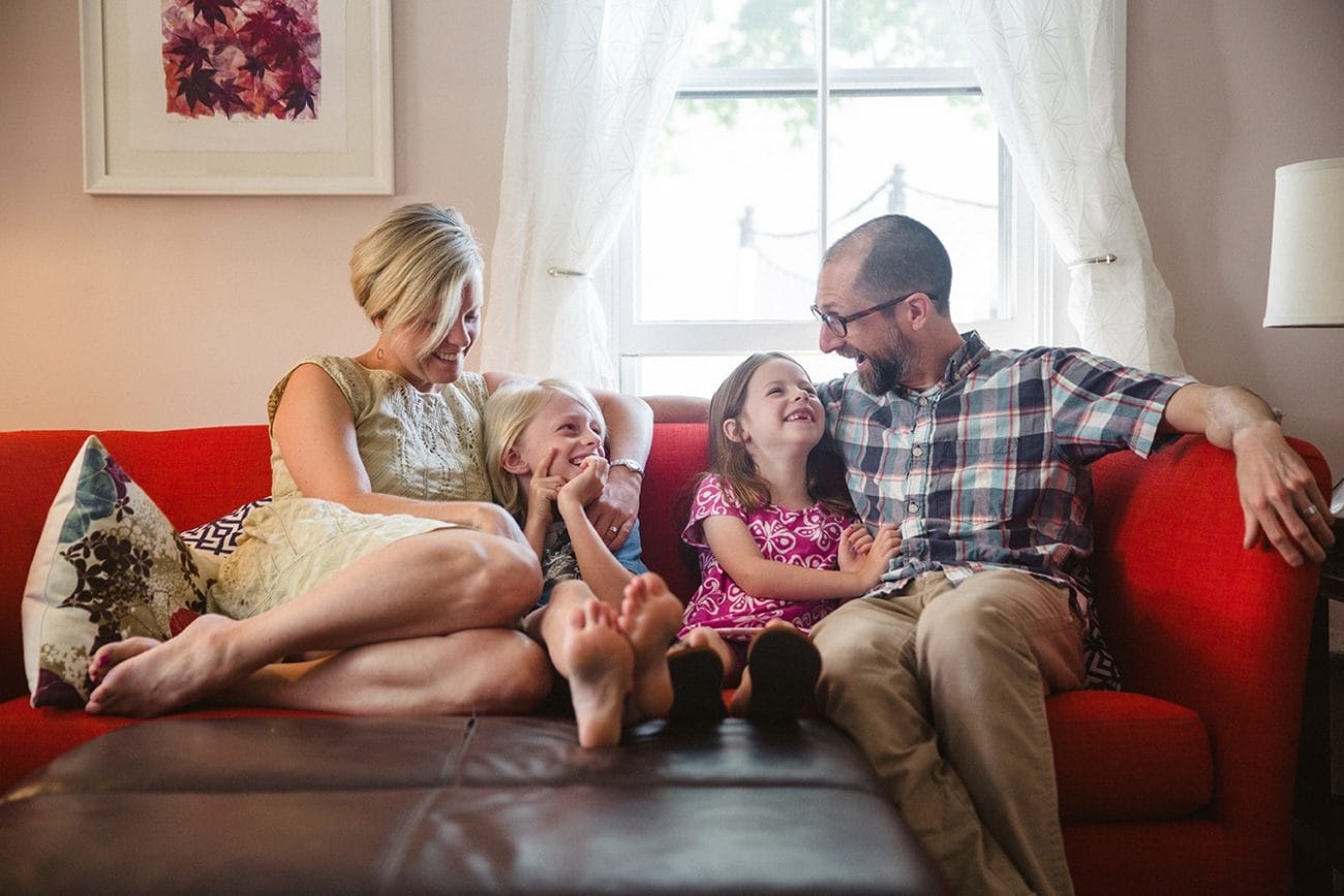 A documentary photograph of a family sitting on the couch together during a family session at home