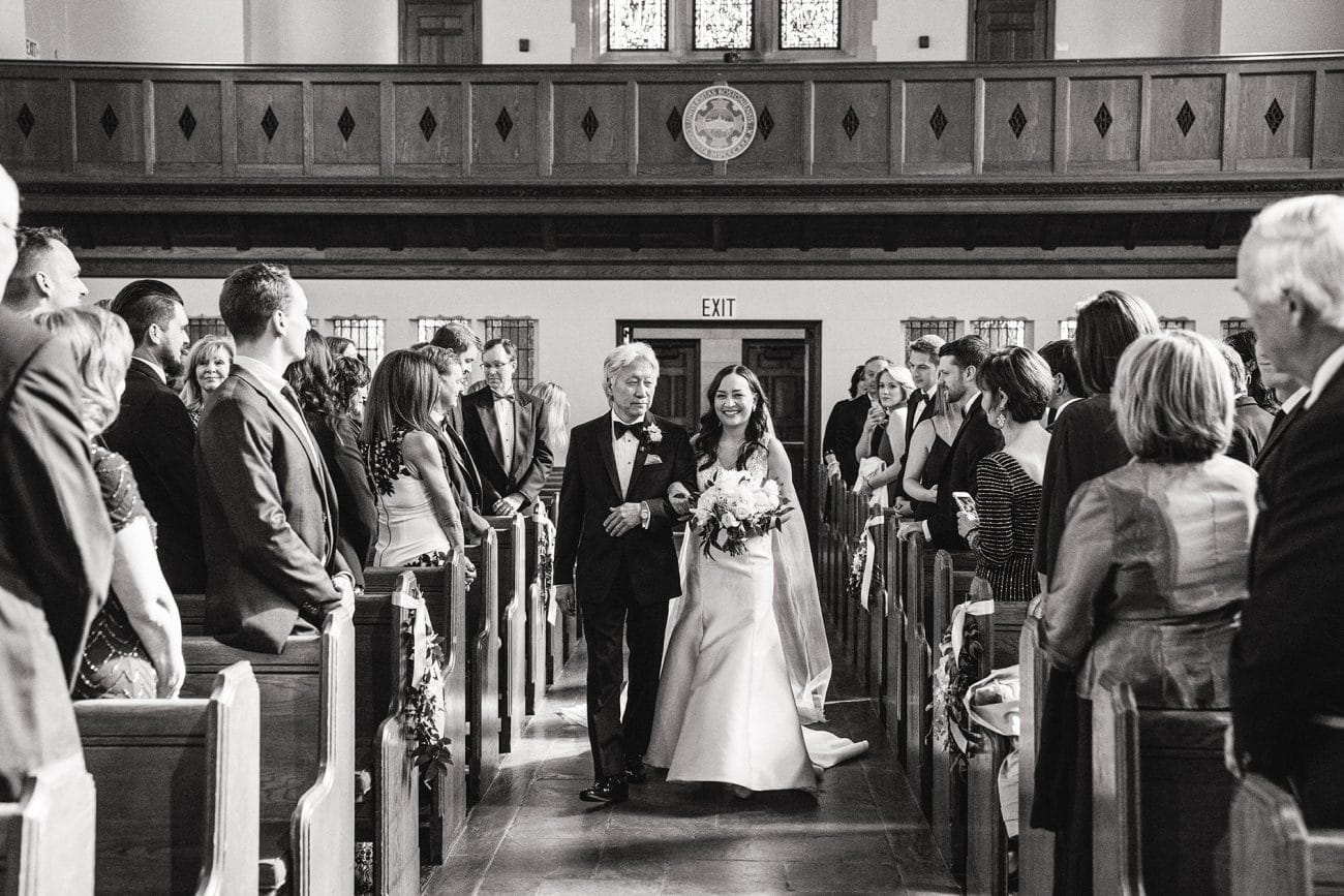 A documentary photograph of a bride walking up the aisle with her father at Marsh Chapel in Boston
