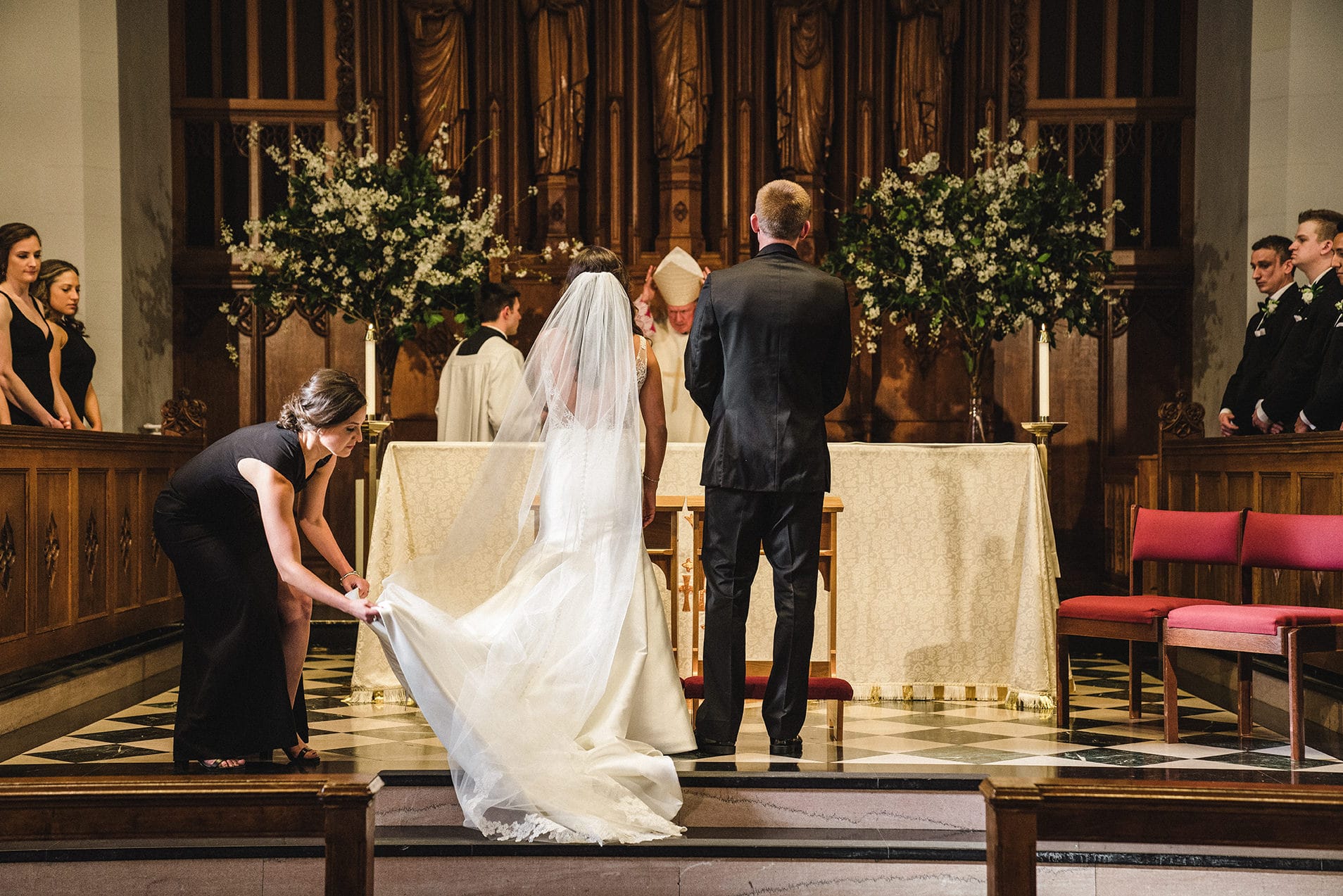 A documentary photograph of a bridesmaid adjusting the bride's train during a Boston Wedding Ceremony at Marsh Chapel