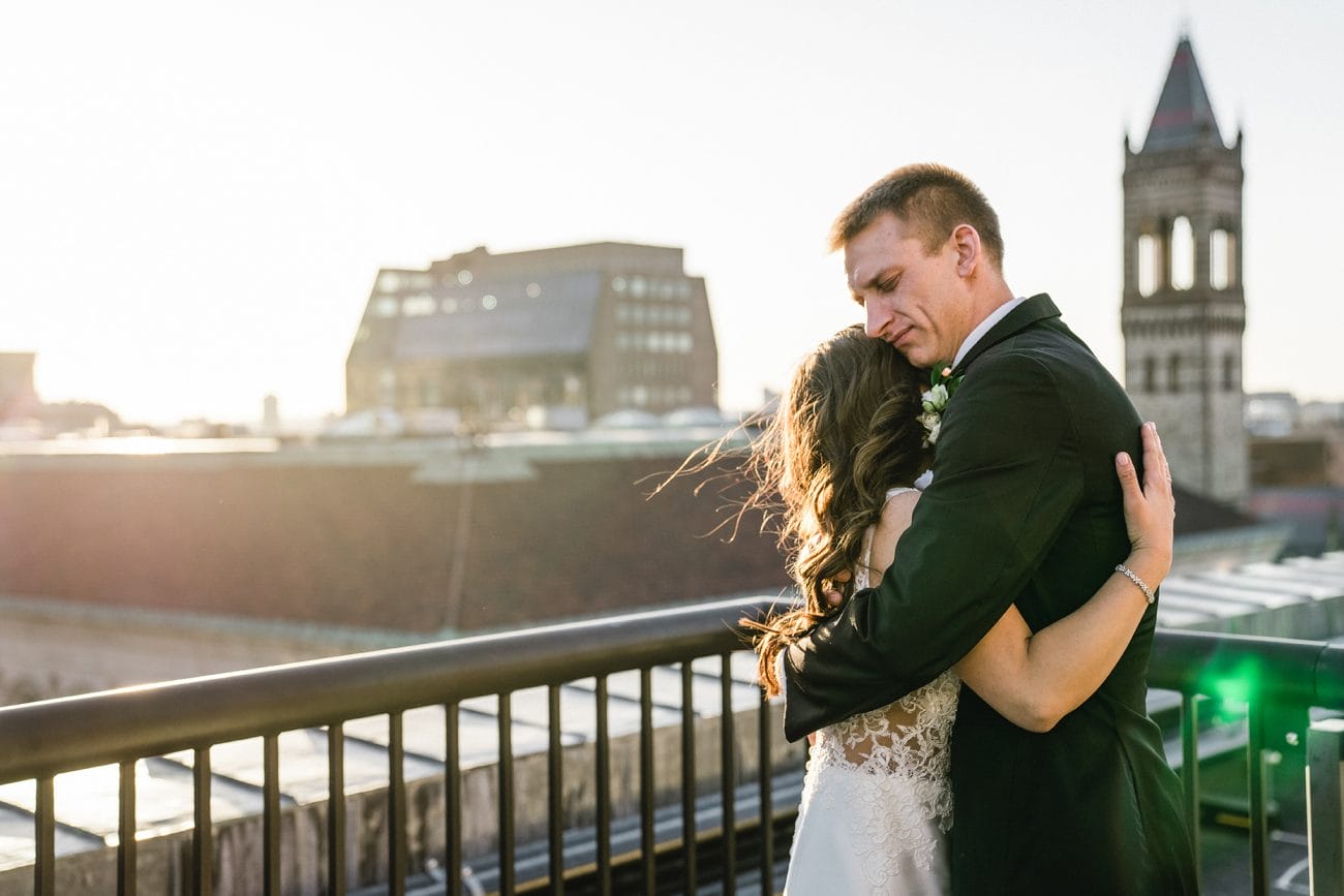 A documentary photograph of a bride and groom hugging on the roof of fairmont copley during their wedding in boston