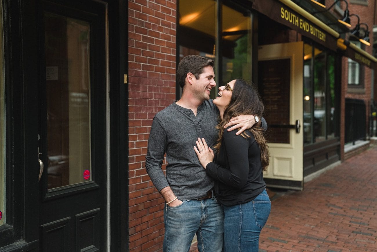 A documentary photograph of a couple laughing outside South End Buttery during their Boston Engagement Session