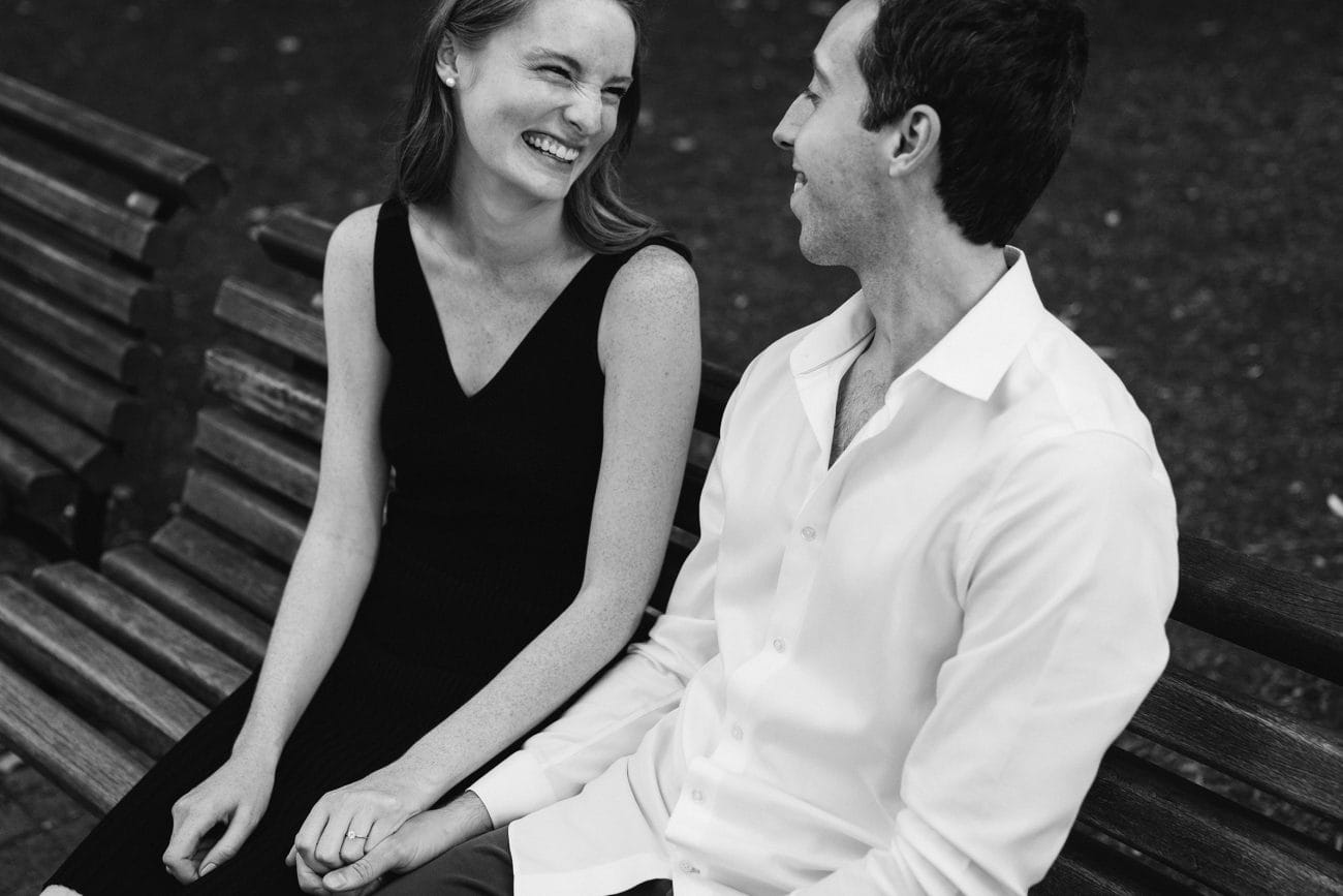 A documentary photograph of a couple talking and laughing on a bench during their Boston engagement session