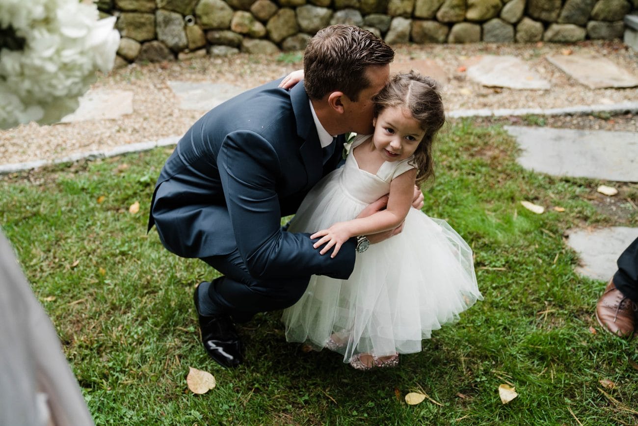 A documentary photograph of a groom kissing the flower girl on the cheek after his Boston wedding ceremony