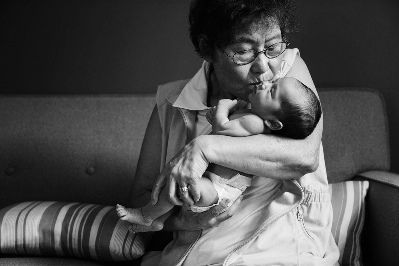 A documentary portrait of a grandmother kissing her newborn granddaughter during an in home newborn session in Boston's Jamaica Plain