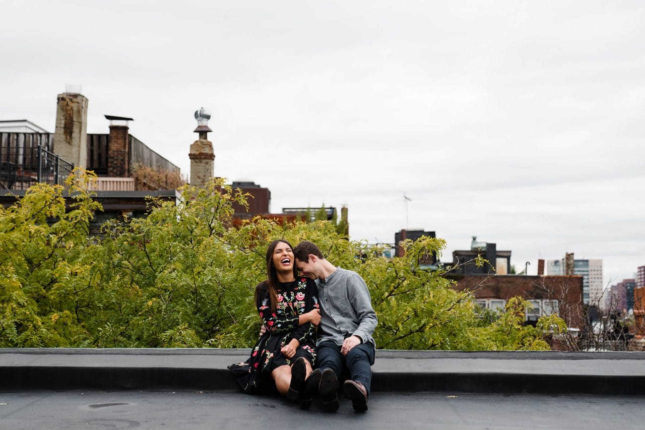 A documentary photograph of a couple laughing together on the roof of their beacon hill apartment during their boston engagement session