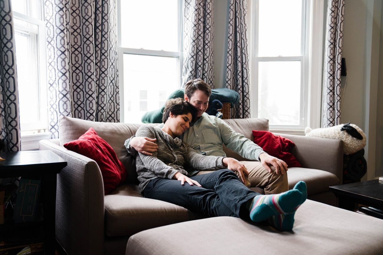 A documentary photograph of a couple cuddling on the couch during their couple session at home