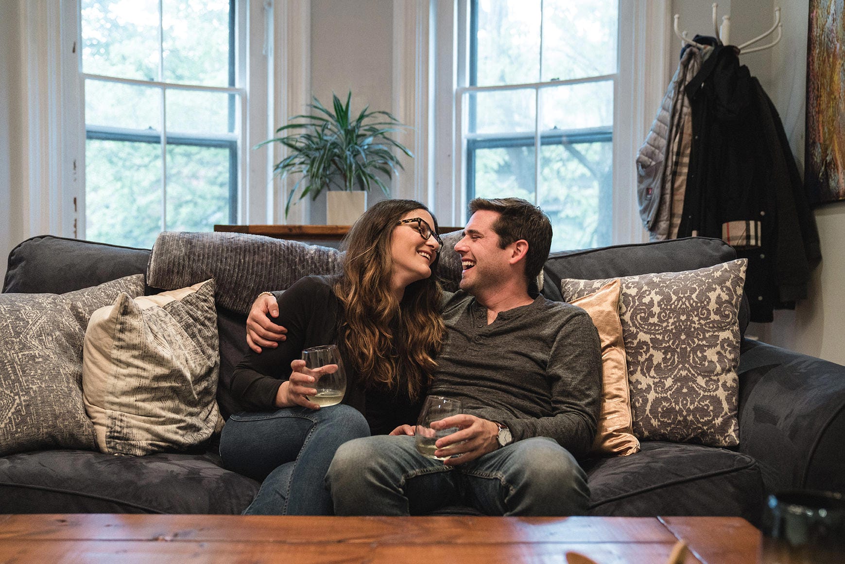 A documentary photograph of a couple laughing together on their couch during an in home boston engagement session