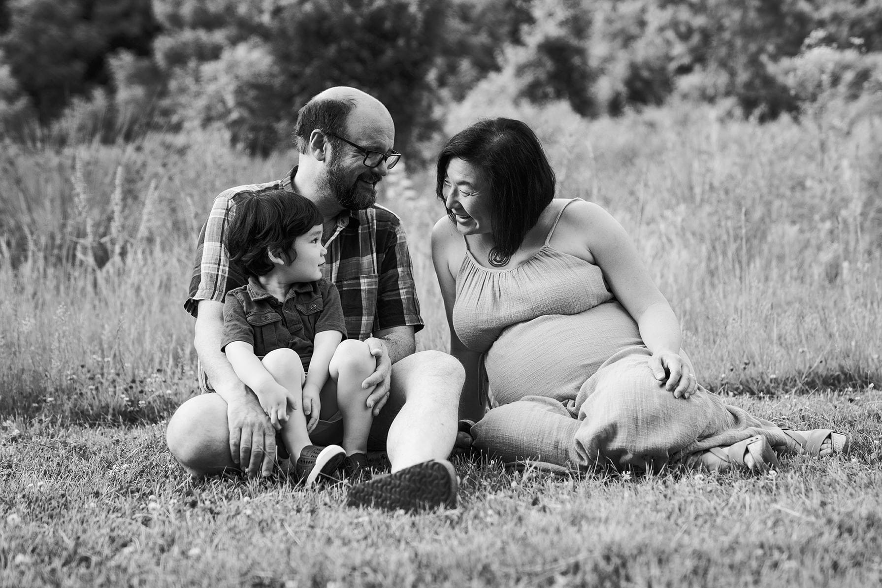 A best of Boston family photograph of a family sitting in the grass during a lifestyle maternity family session in Boston