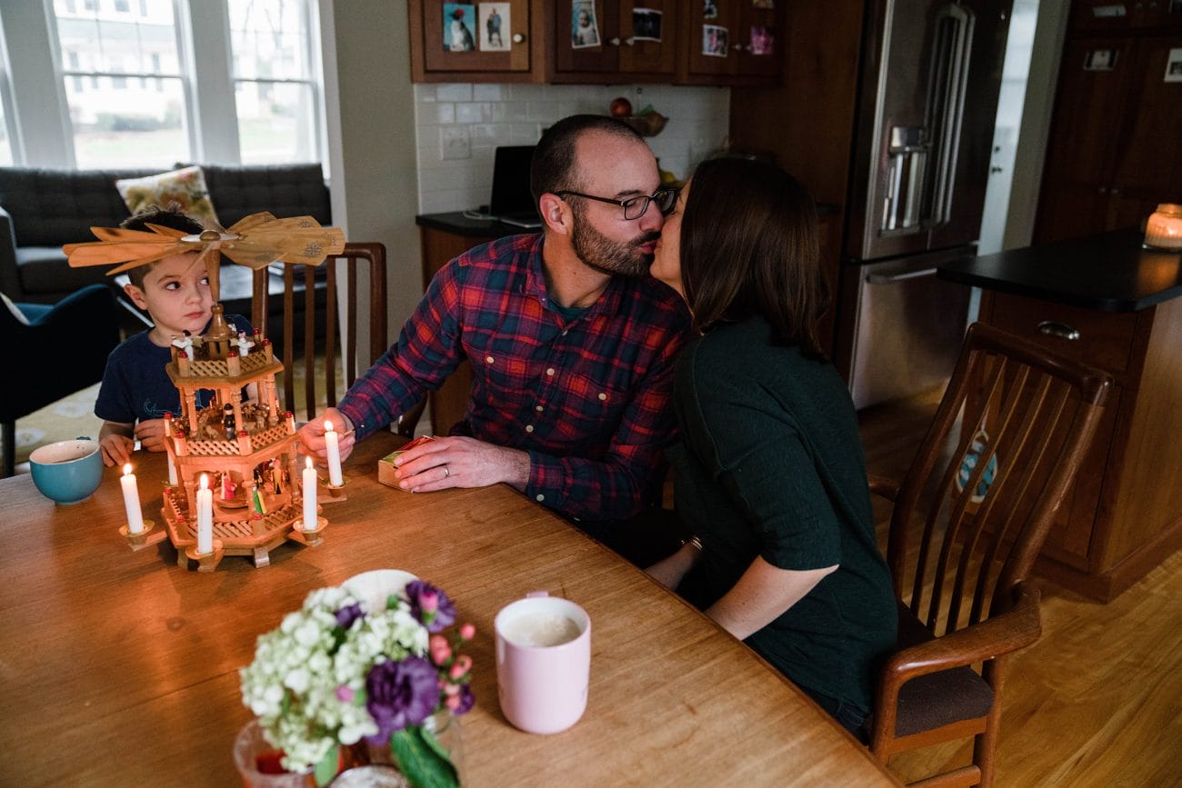 A best of Boston family photograph of parents kissing while they set up the Christmas decorations with their son during an in home family session in Boston