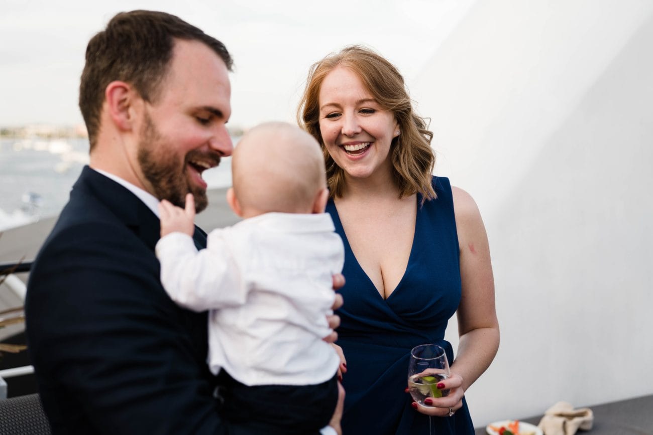A best of Boston wedding photograph of a couple and their baby enjoying the cocktail hour during a wedding on the Odyssey in Boston's seaport