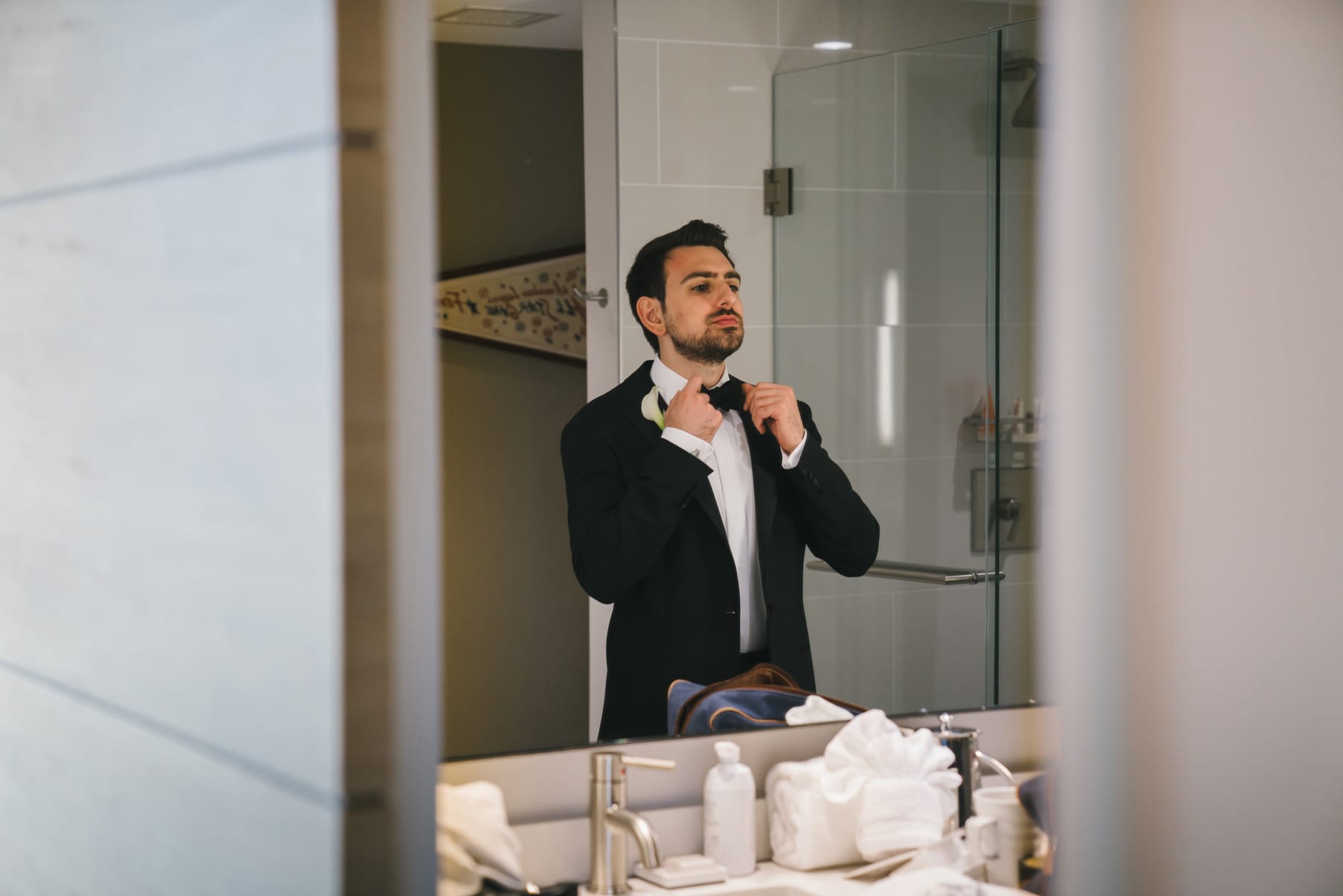 A best of Boston wedding photograph of a groom adjusting his bowtie before his Commonwealth Hotel wedding in Boston