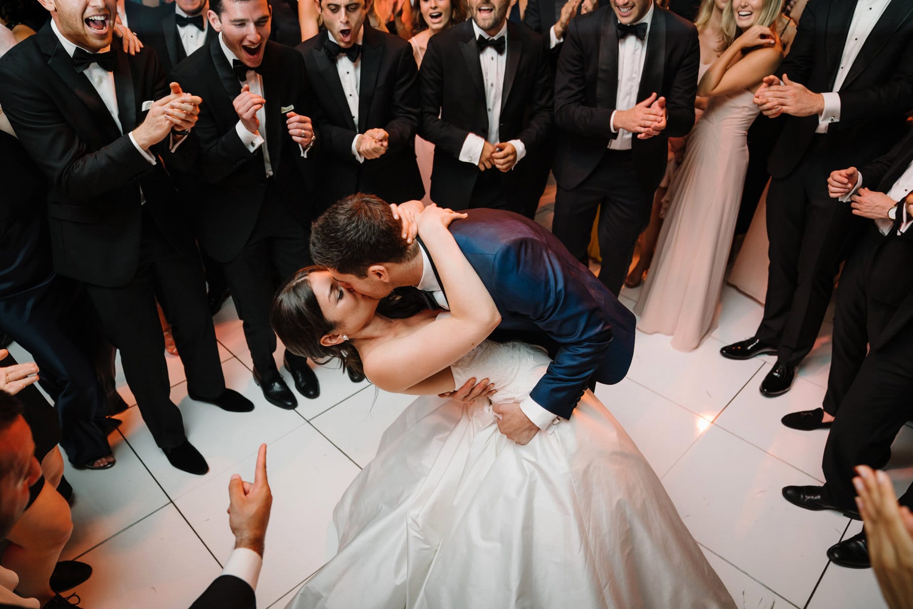A best of Boston wedding photograph of bride and groom kissing on the dance floor surrounding by friends during a Four Seasons wedding in Boston