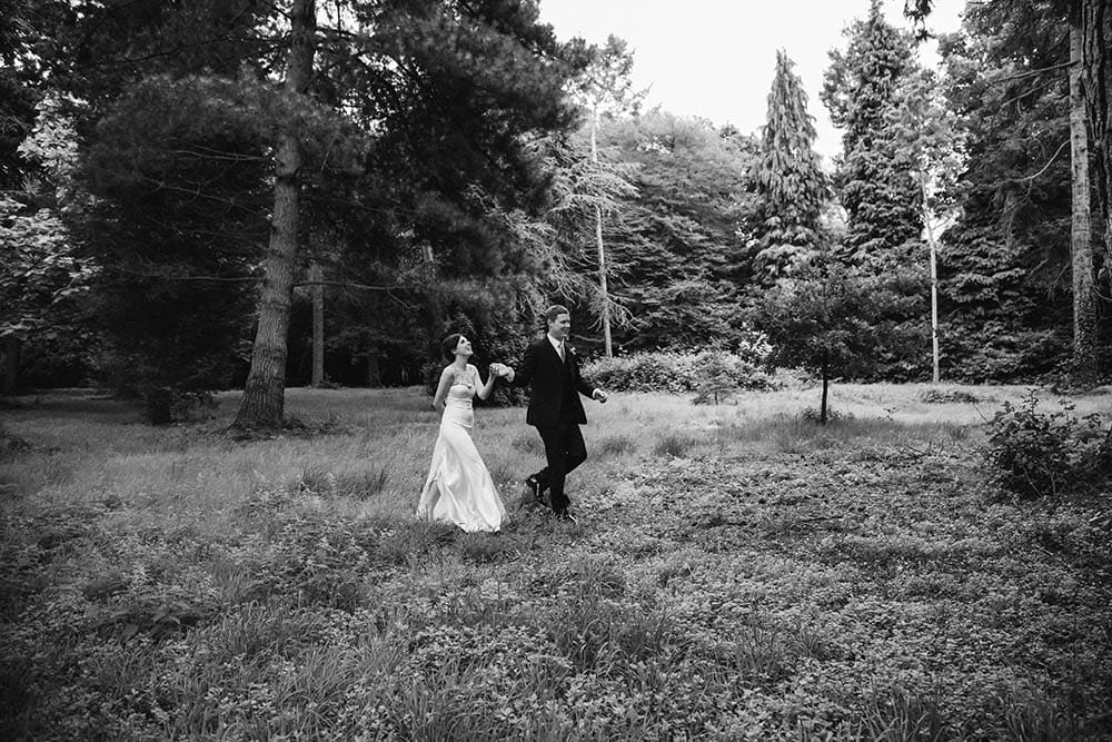 A documentary photograph of a bride and groom walking through a field during their Boston wedding