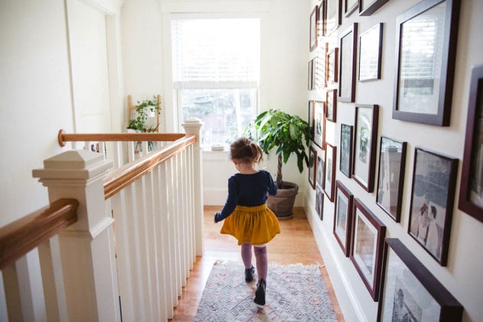 A documentary photograph of a girl running down the hallway during an in home family session in Boston's Jamaica Plain area