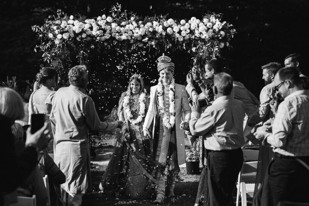 A documentary photograph featured in the best of wedding photography of 2019 showing a couple walking down the aisle with flower petals being thrown during their Indian wedding ceremony