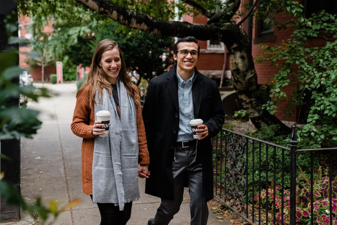 A documentary photograph of a couple walking down the street, coffee in hand, during a date night engagement session in Boston