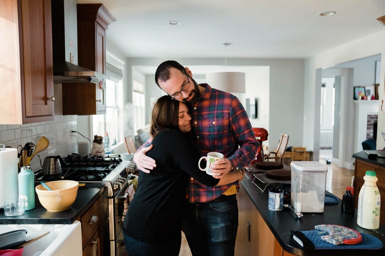 A best of Boston family photograph of parents hugging while their son plays in the background during an in home family session in Boston