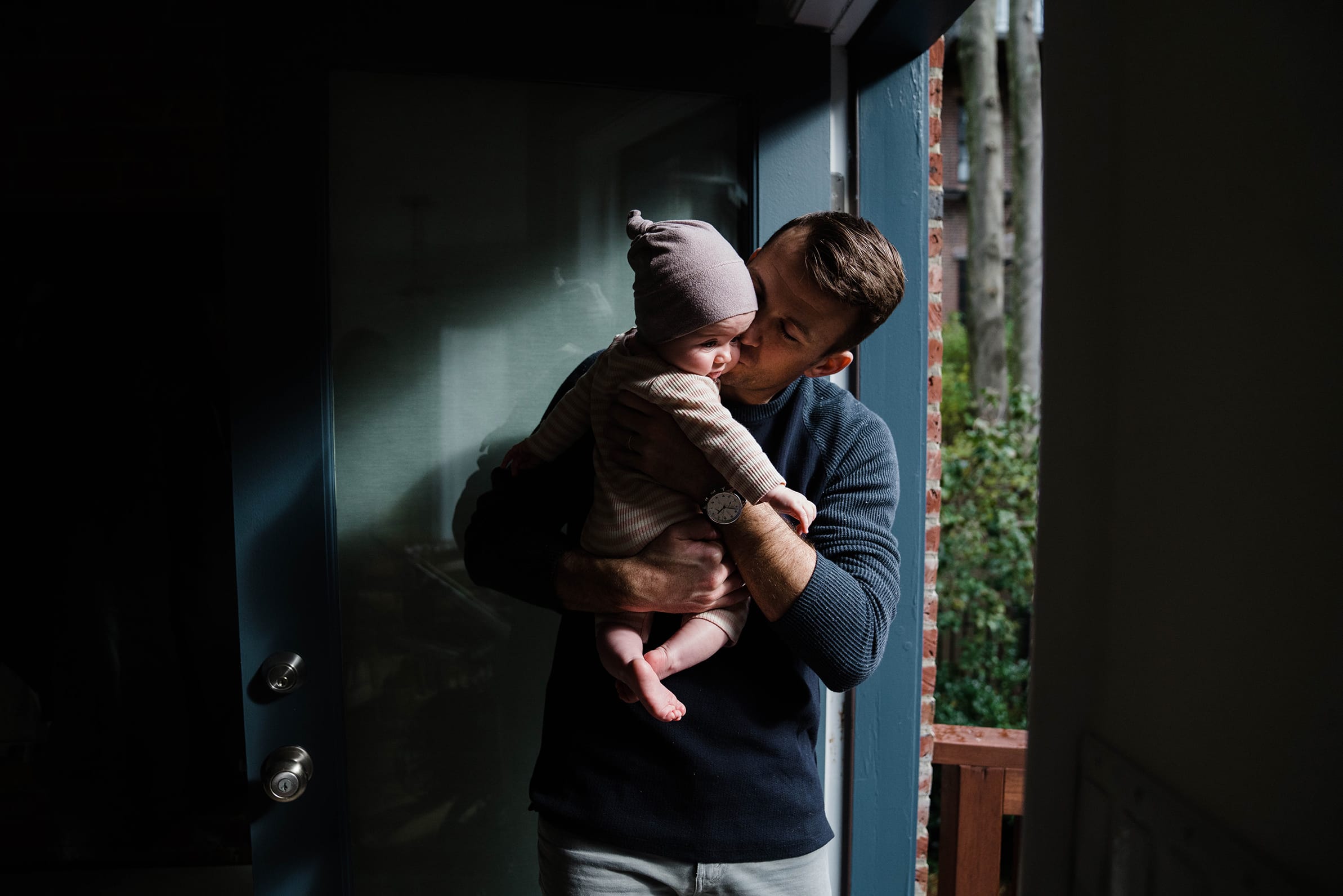 A documentary photograph of a father kisses his baby girl during an in home family session in Boston