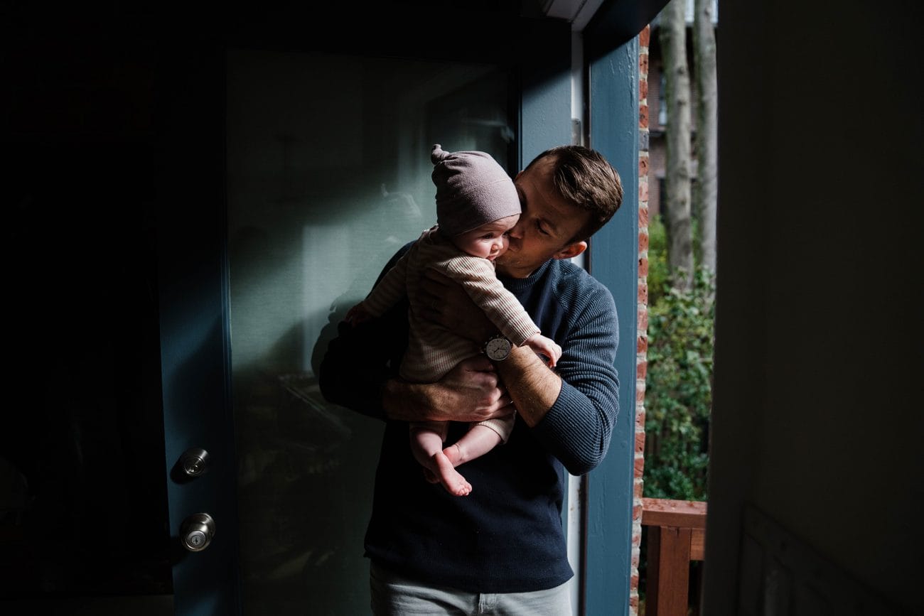 A documentary photograph of a father kisses his baby girl during an in  home family session in Boston