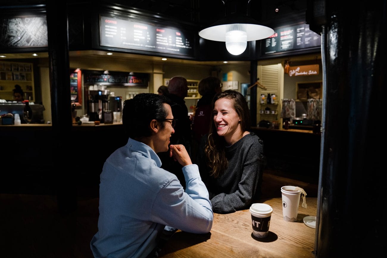 A documentary photograph of a couple laughing together at Pavement coffee shop during their date night engagement session in Boston