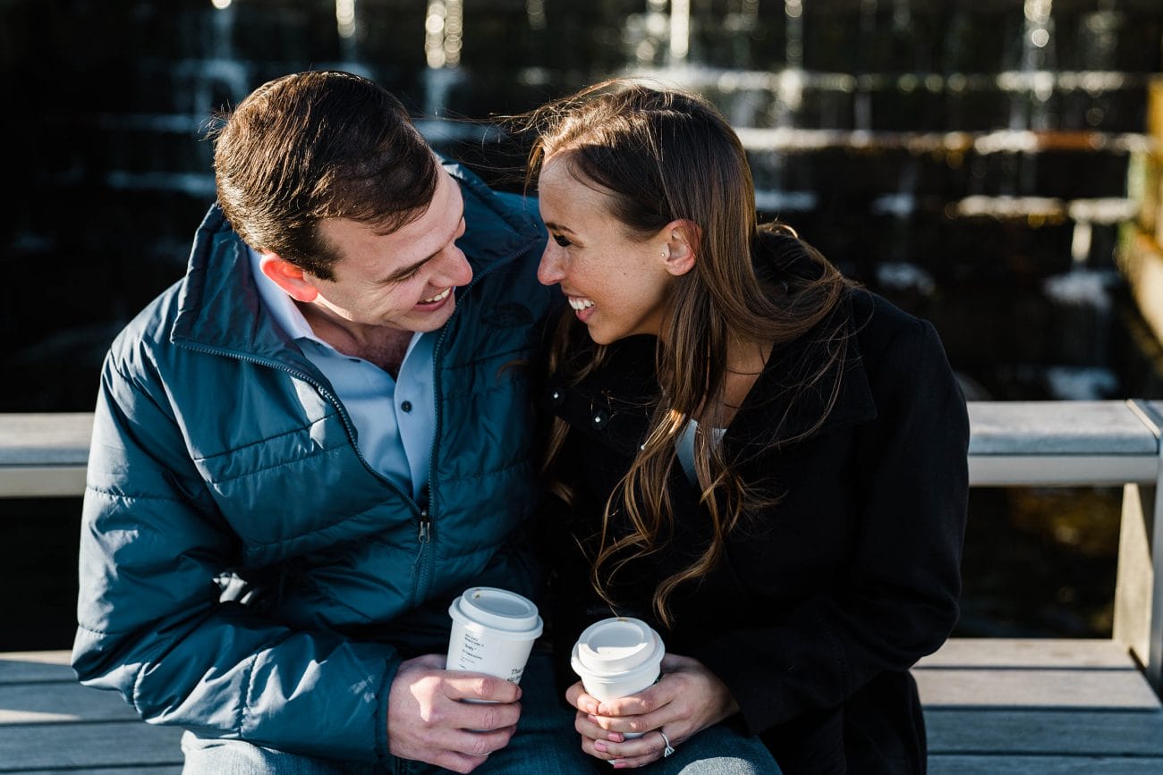 A documentary photograph of a couple laughing together while they drink coffee during their sunrise engagement session
