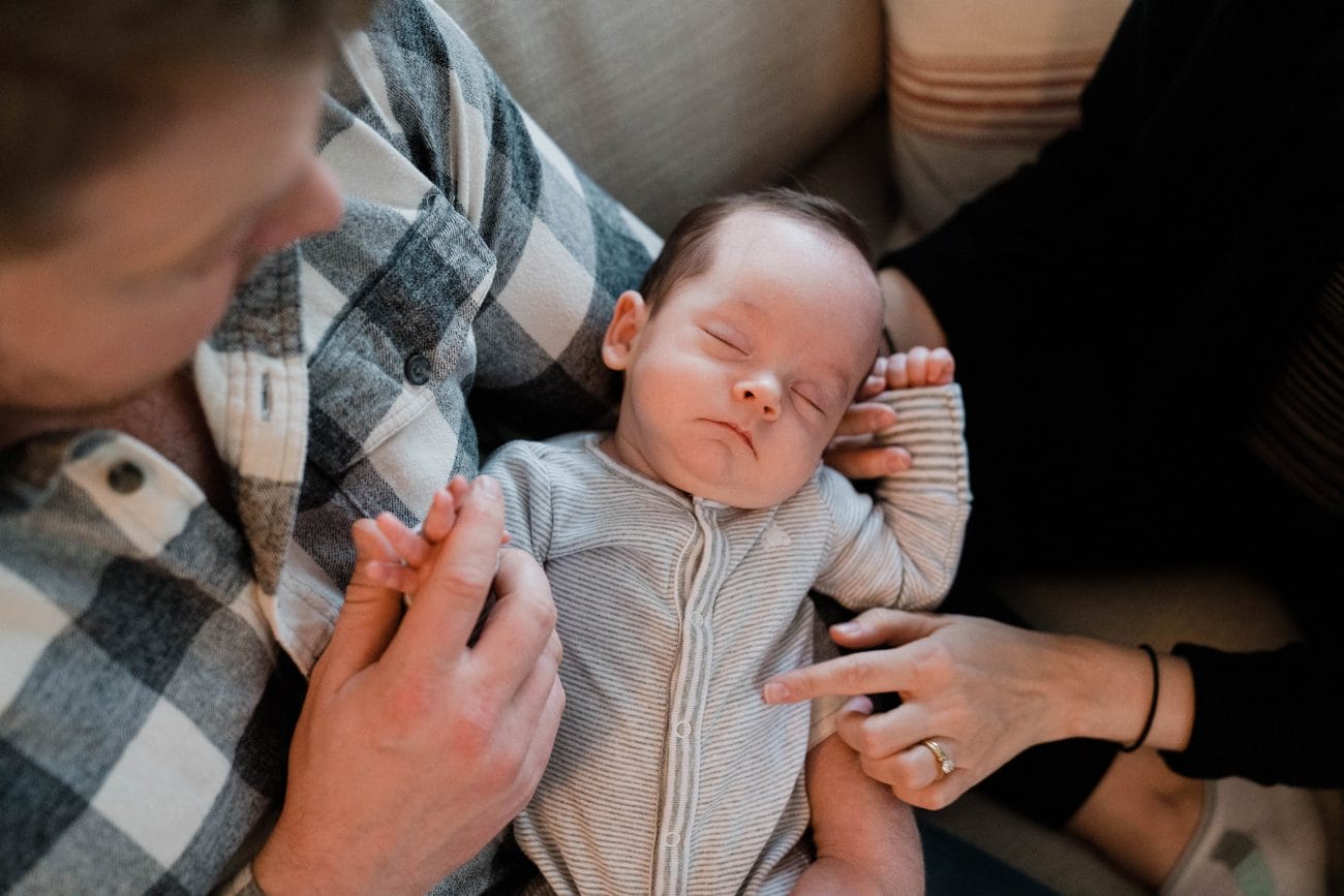 A documentary photograph of baby sleeping in his father's arms during an in home family session in Boston