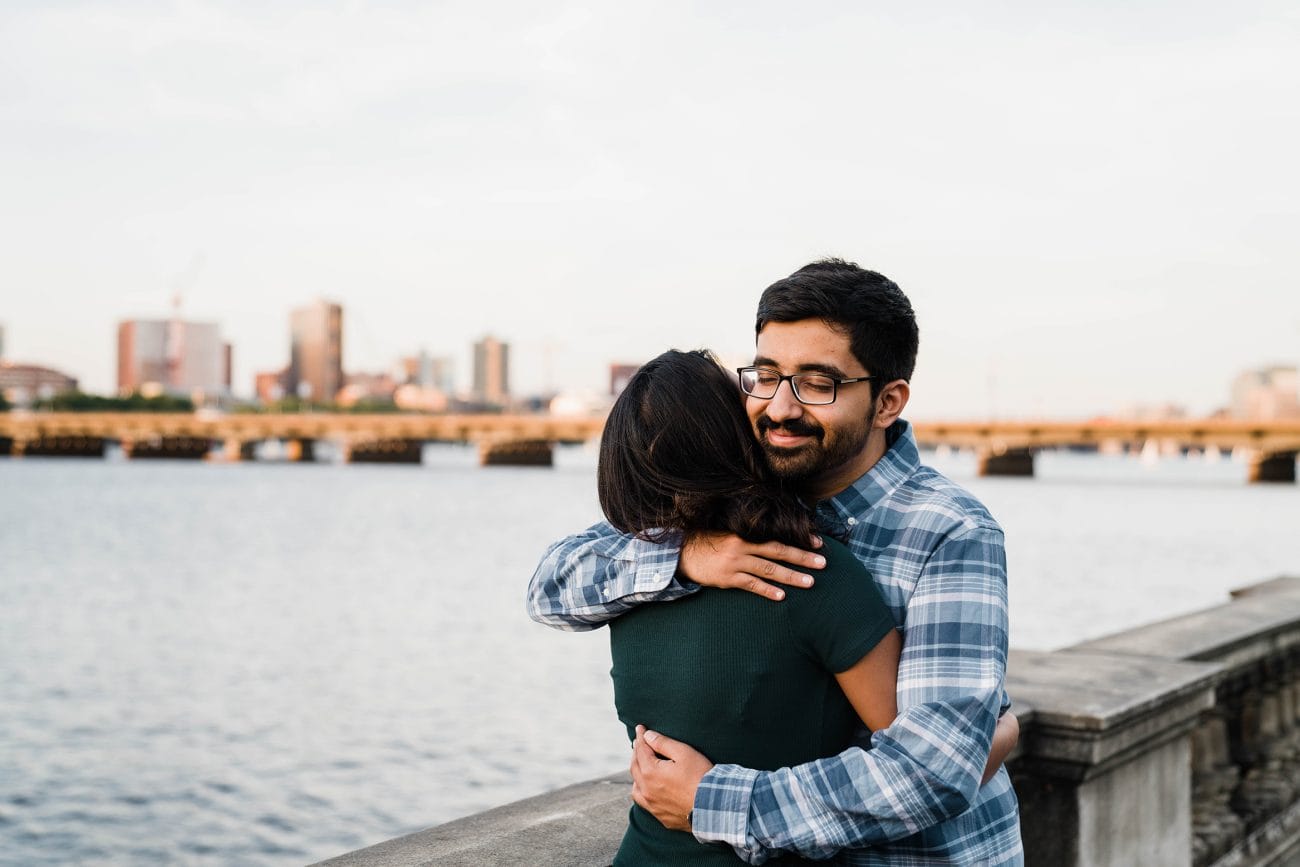 A documentary photograph of a couple hugging each other near the Charles River during a date night engagement session in Boston