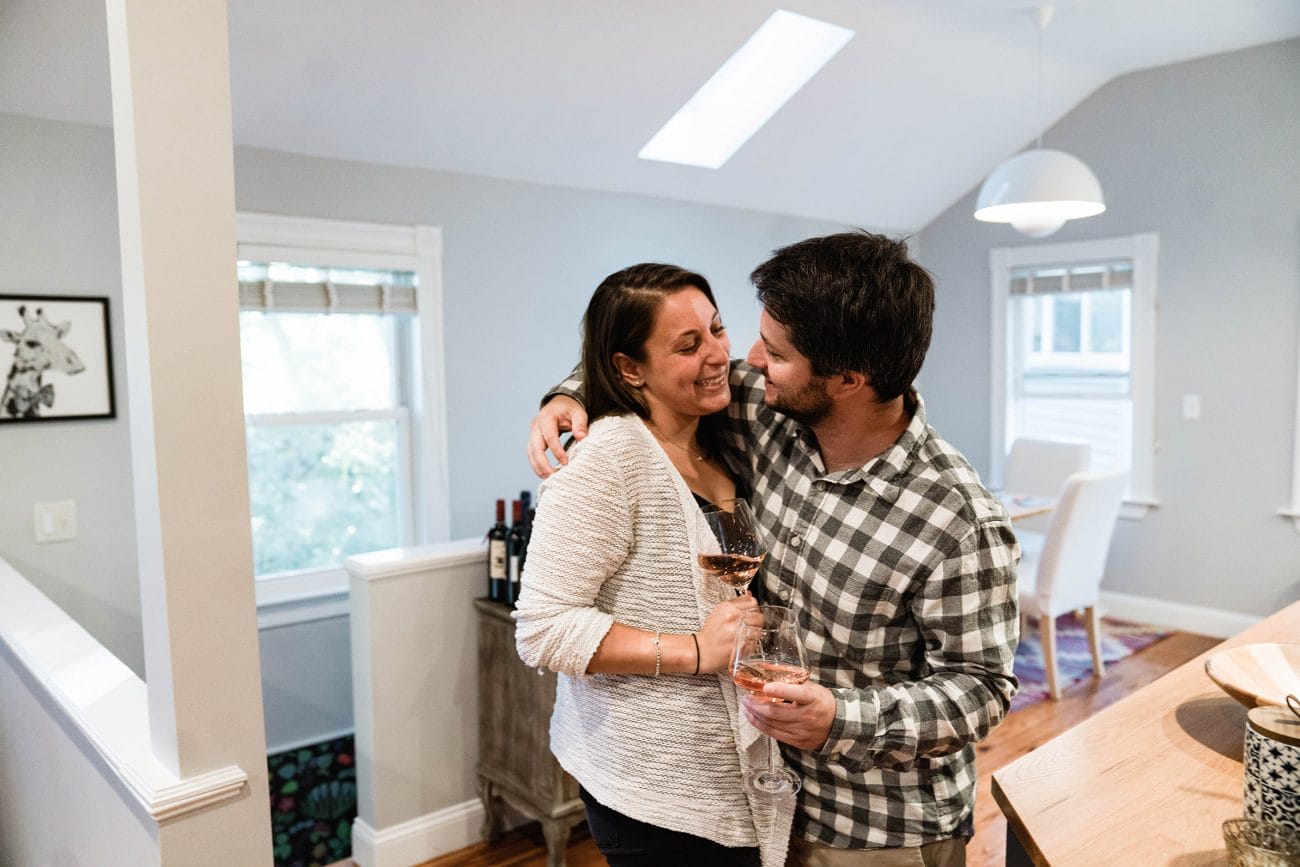 A documentary photograph of a couple about to kiss with wine in hand during their in home engagement session in Boston