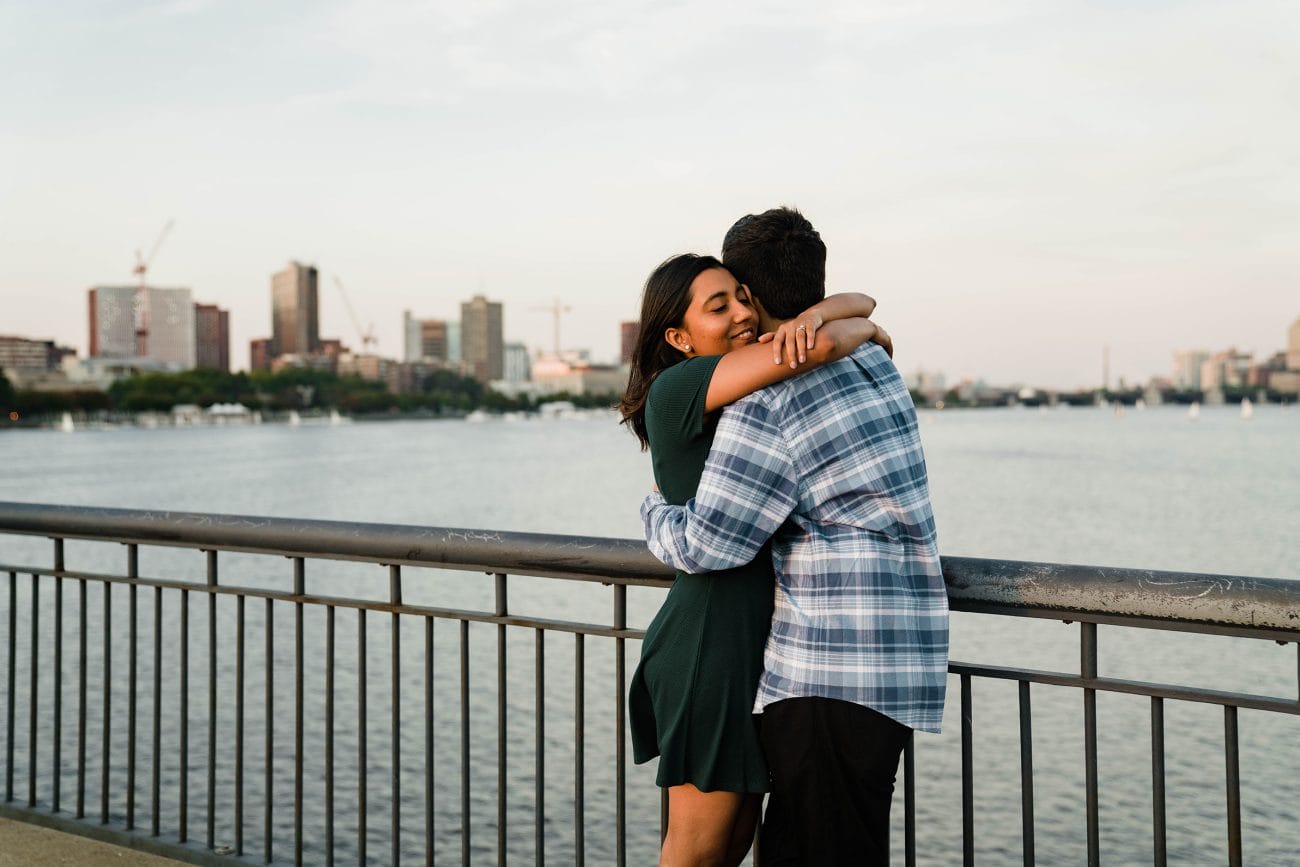 A documentary photograph of a couple hugging near the Charles River during their date night engagement session in Boston