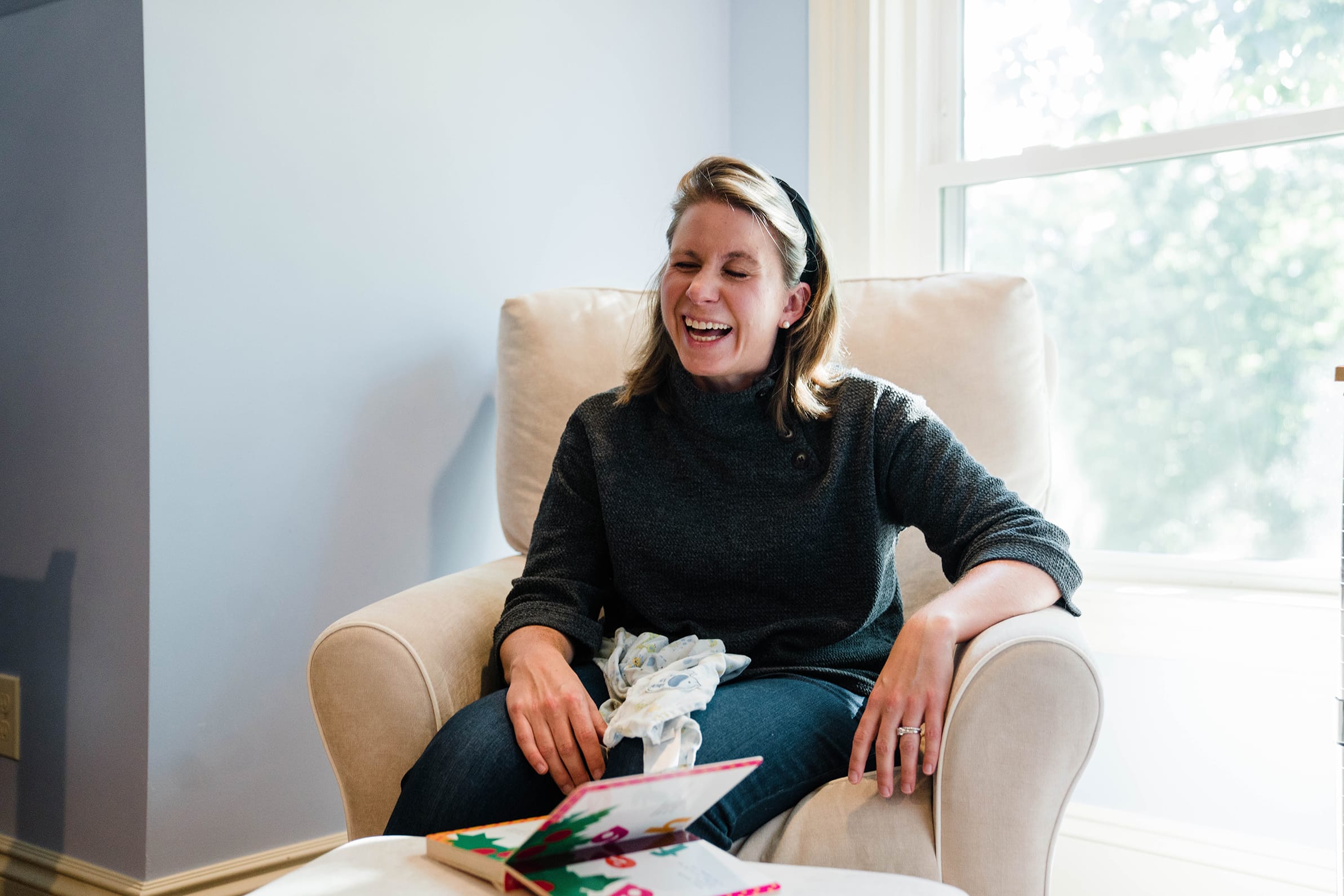A documentary photograph of mom laughing while she watches her son's play during a in home family session in Boston