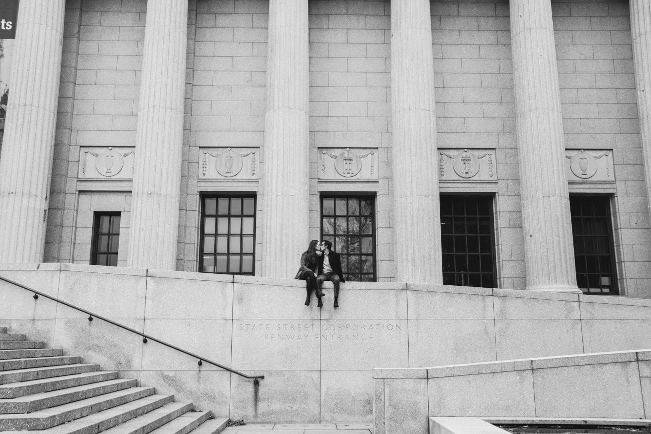 A documentary photograph of a couple sitting on the wall of the Boston Museum of Fine Arts during a date night engagement session